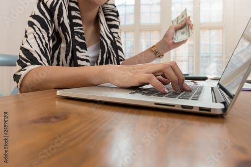 Business and finance concept, Businesswoman holding cash and using laptop for E-Commerce online shopping.