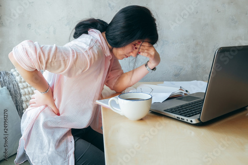 Tired upset young businesswoman suffering from strong chronic backache or osteochondrosis at work, stressed student girl feels pain in aching back photo