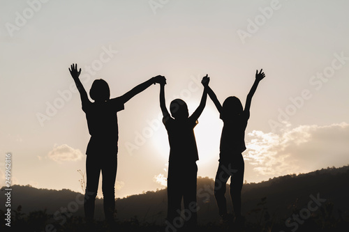 Silhouette group children with raised hands playing on mountain at sunset time.