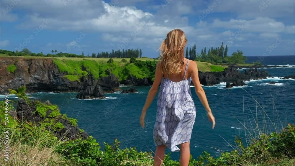Young lady in summer dress stands on the cliff edge and enjoys coastal view at sunny windy day. Young lady in summer dress stands on the cliff edge and enjoys coastal view at sunny windy day.