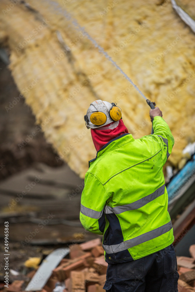 Workman spraying water over a demolition site to prevent dust and possible fire from the demolition process Workman spraying water over a demolition site to prevent dust and possible fire from the demolition process