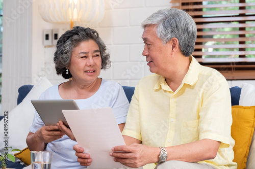 Asian senior couple use tablet searching about retirement financial document sitting on sofa at home,senior learn to use technology.aging in place concept.
