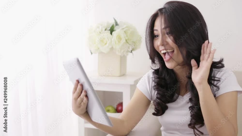 happy young asian woman using tablet computer doing video call while relaxing at home happy young asian woman using tablet computer doing video call while relaxing at home