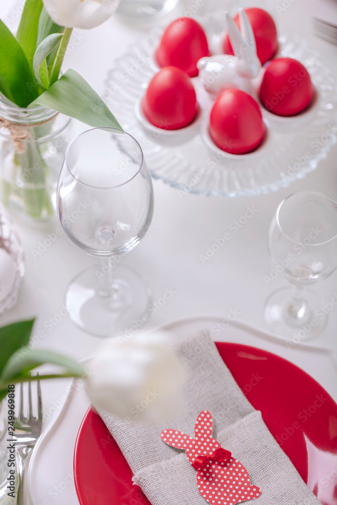 Happy easter. Decor and table setting of the Easter table is a vase with white tulips and dishes of red and white color. Easter colored eggs with white polka dots. Happy easter. Decor and table setting of the Easter table is a vase with white tulips and dishes of red and white color. Easter colored eggs with white polka dots.