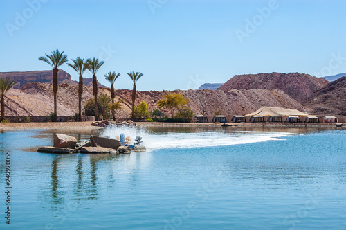 Timna Lake surrounded by camping areas, resting zones, growing palms and ancient cooper mines canyons and mountains range in Timna National Park in the middle of a desert in Southern Israel