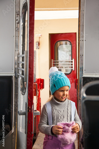 Little girl in blue cap and winter pants tarvelling by old train Kukushka in Georgia between Bakuriani and Borjomi photo