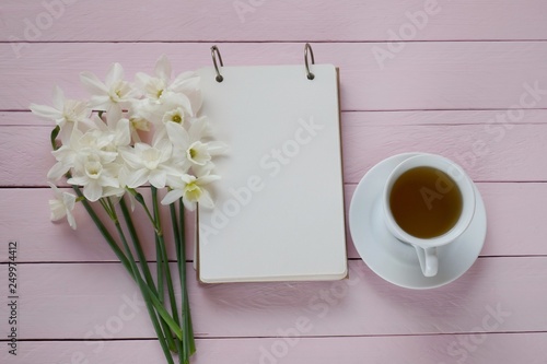 Spring tea.Flat lay.Spring to-do list.cup of tea  notebook  white daffodils bouquet on pink board wooden background..top view  copy space.Spring mood