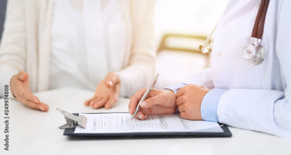 Unknown woman doctor and female patient discussing something while standing near reception desk in emergency hospital. Physician at work in clinic. Medicine and health care concept Unknown woman doctor and female patient discussing something while standing near reception desk in emergency hospital. Physician at work in clinic. Medicine and health care concept
