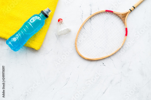 Badminton training concept. Badminton racket, shuttlecock, sport drink and towel on white stone background top view copy space