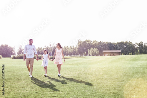 Family walk. Family of three walking on grassy field smiling hap