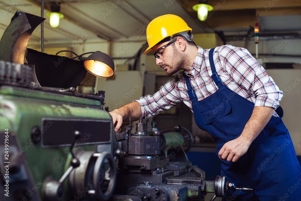 Worker in uniform operating in manual lathe in metal industry factory Worker in uniform operating in manual lathe in metal industry factory