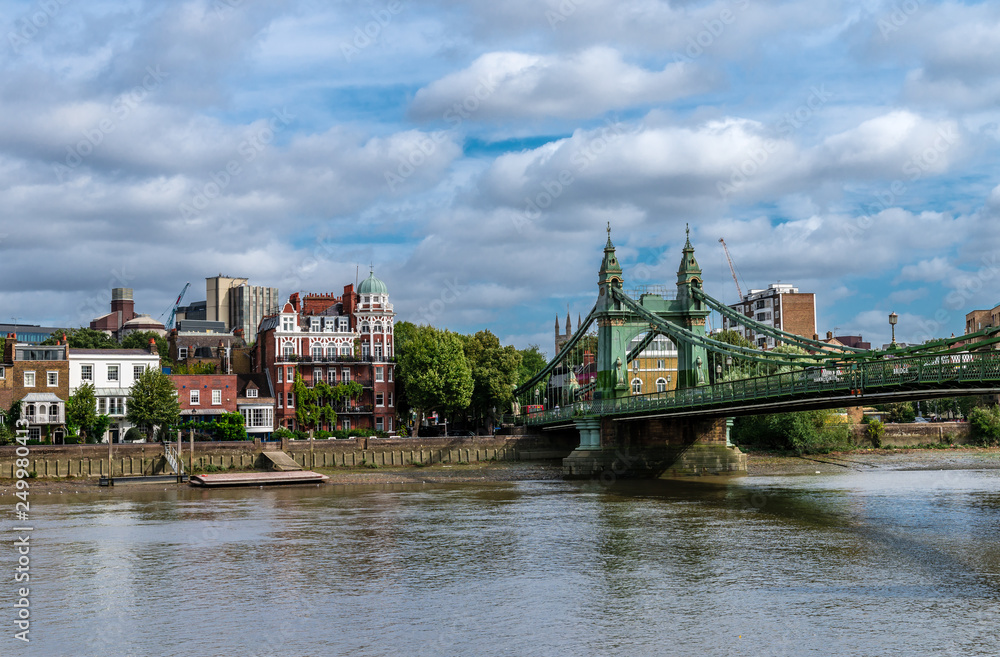 Fototapeta premium The Hammersmith Bridge, a suspension bridge that crosses the River Thames in west London. Hammersmith is in the background, photo taken from Barnes.