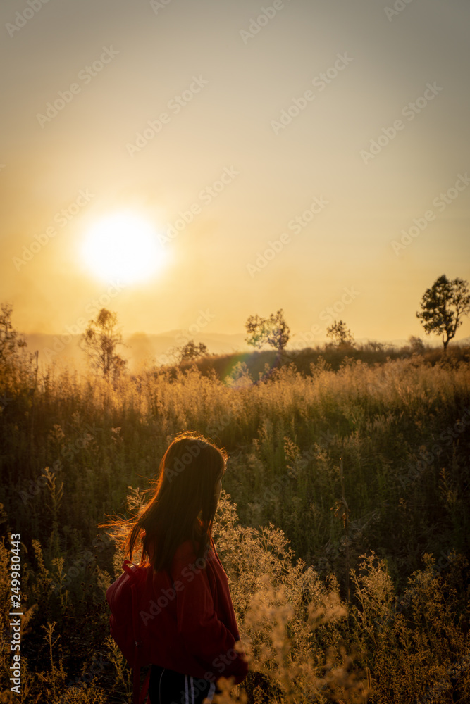 The girl travels in the grass field at sunset.