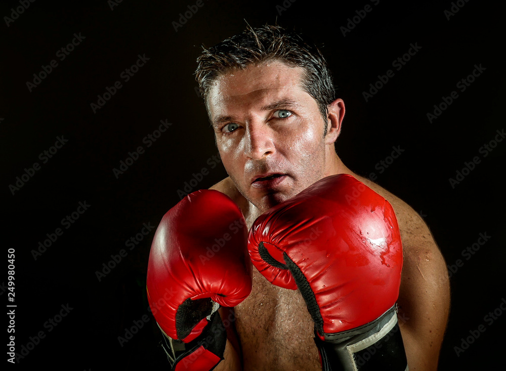 young angry and fierce sport man in boxing gloves posing in badass fighter attitude cool and furious in boxer stance isolated on black background in dramatic studio light