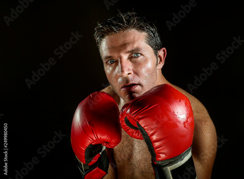 young angry and fierce sport man in boxing gloves posing in badass fighter attitude cool and furious in boxer stance isolated on black background in dramatic studio light