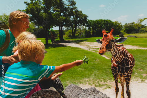 Canvas Print father and kids feeding giraffes in zoo