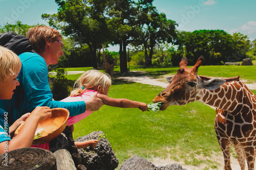 father and kids feeding giraffes in zoo photo