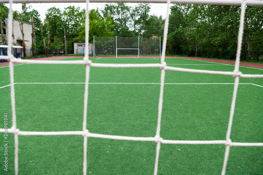 View through the net at artificial turfed playing field and white football goal View through the net at artificial turfed playing field and white football goal