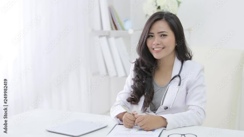 happy female doctor smiling to the camera while working on her desk happy female doctor smiling to the camera while working on her desk
