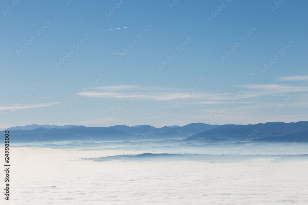 Fog filling a valley in Umbria (Italy), with layers of mountains and hills, various shades of blue and Montefalco town at the distance