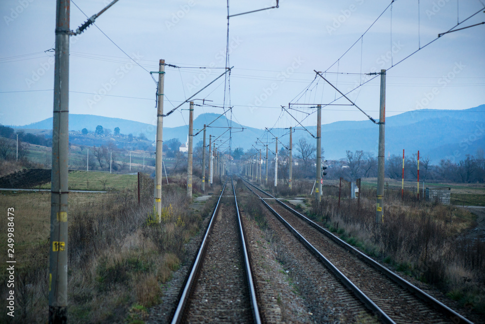 Eastern European railroad across Transilvania. Mountain landscape in the background. Scary, dangerous scene in winter with naked trees and polluted nature 