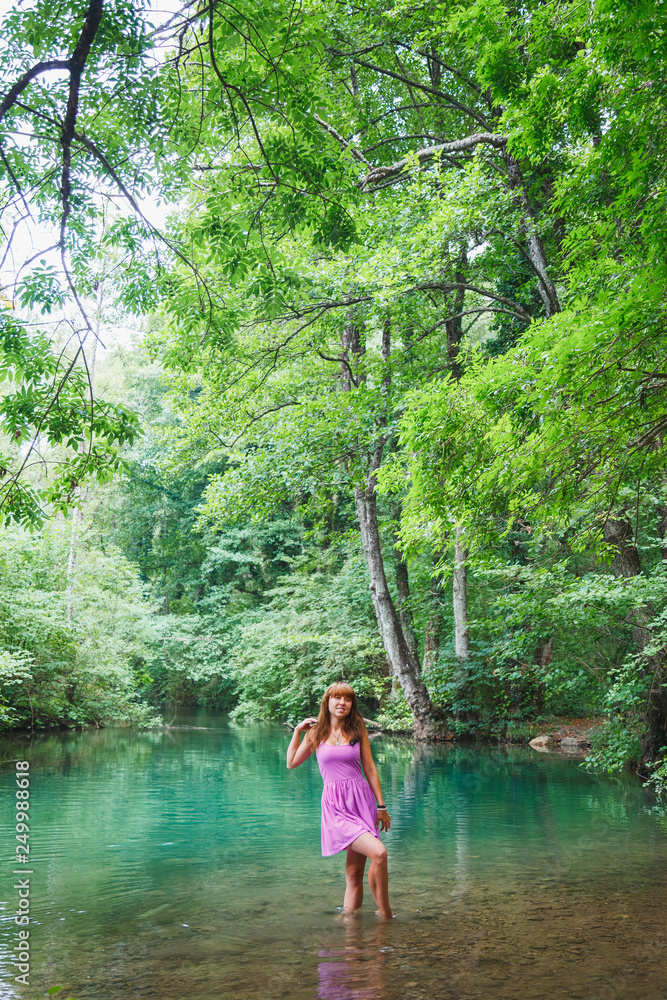 Fototapeta premium girl in a pink short dress walks on a river in the forest