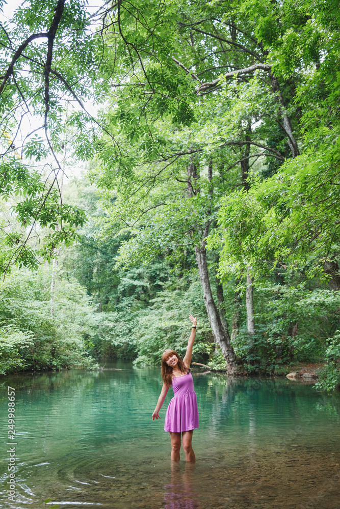 Fototapeta premium girl in a pink short dress walks on a river in the forest