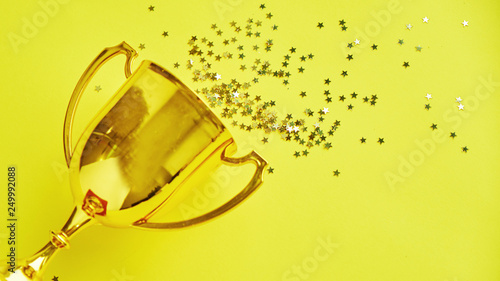 Champion gold cup trophy on yellow background. minimalism style, victory celebration concept. and golden stars of confetti are scattered around