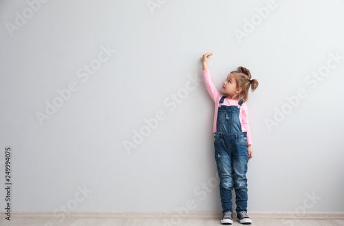 Portrait of cute little girl near light wall