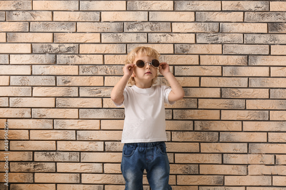 Portrait of cute little boy with sunglasses on brick background