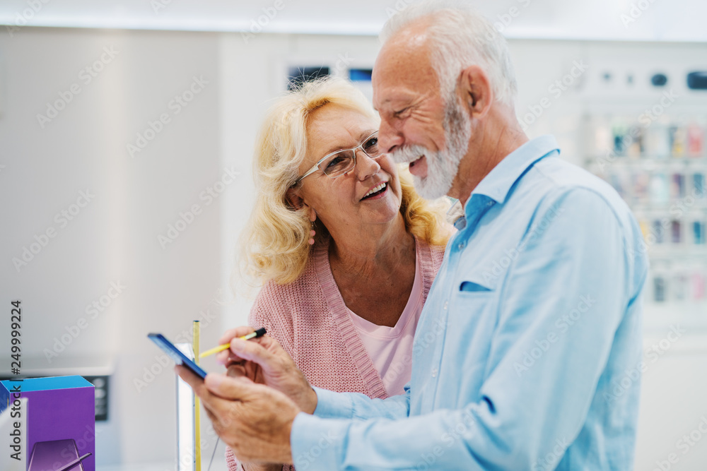 Close up of smiling old couple trying out tablet while standing in tech store. Close up of smiling old couple trying out tablet while standing in tech store.