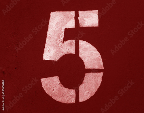Number 5 in stencil on metal wall in red tone.