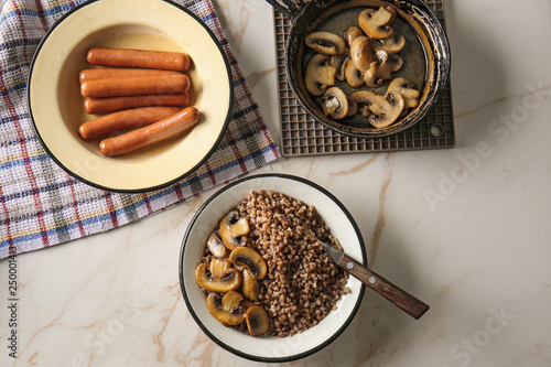 Bowl with tasty boiled buckwheat, fried mushrooms and sausages on table