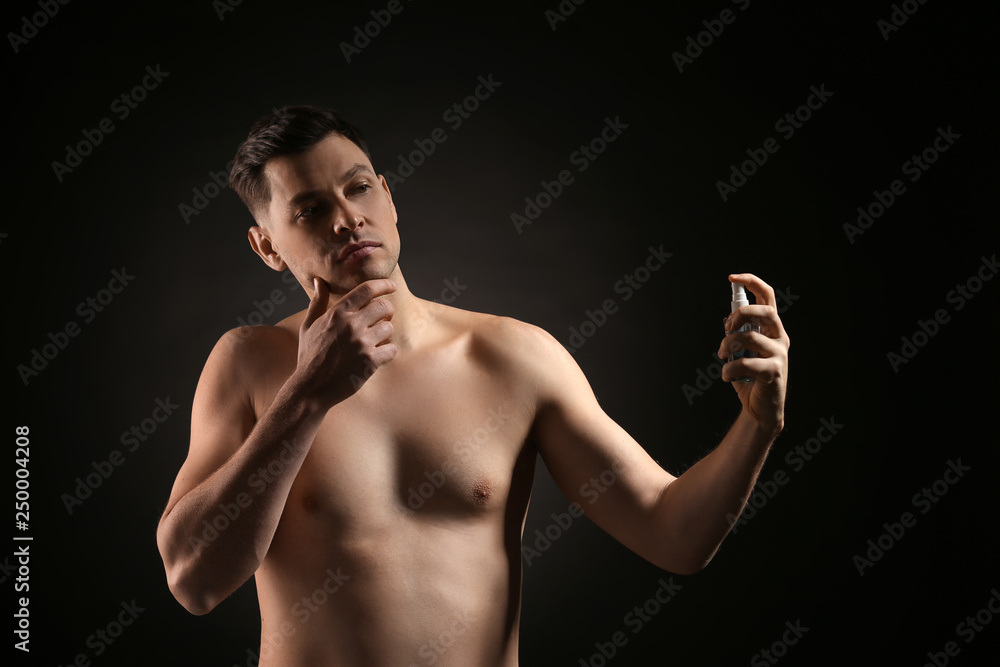 Handsome man with bottle of perfume on dark background Handsome man with bottle of perfume on dark background