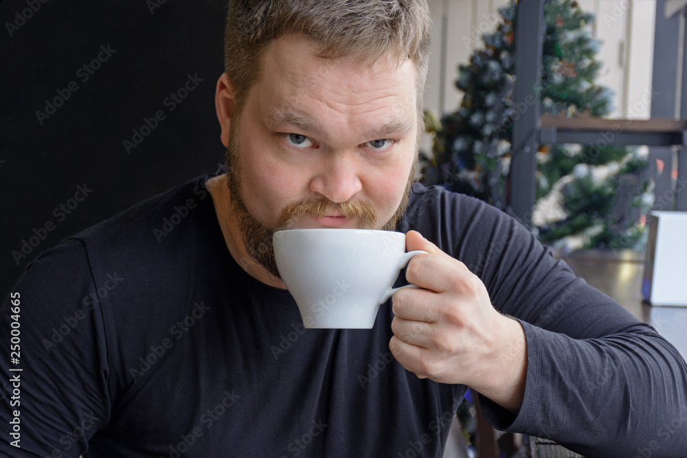 Closeup shot of bearded man drinking coffee and looking at camera. Sitting handsome perfect hairstyle man. Copy space on black background Closeup shot of bearded man drinking coffee and looking at camera. Sitting handsome perfect hairstyle man. Copy space on black background