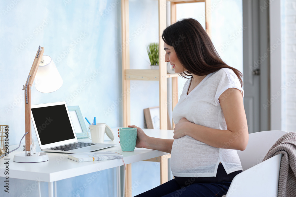 Beautiful pregnant woman using laptop at table Beautiful pregnant woman using laptop at table