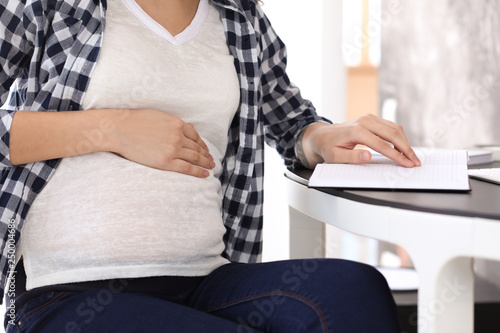 Beautiful pregnant woman with notebook sitting at table