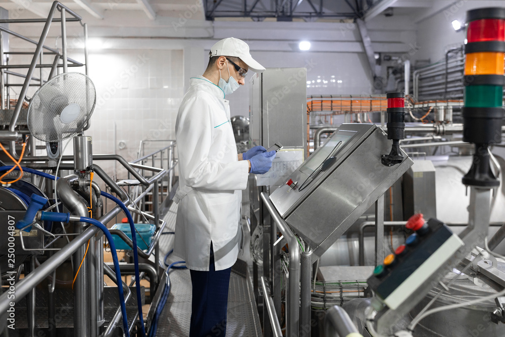 Technologist stands with a tablet near the digital screen at the dairy Plant Technologist stands with a tablet near the digital screen at the dairy Plant
