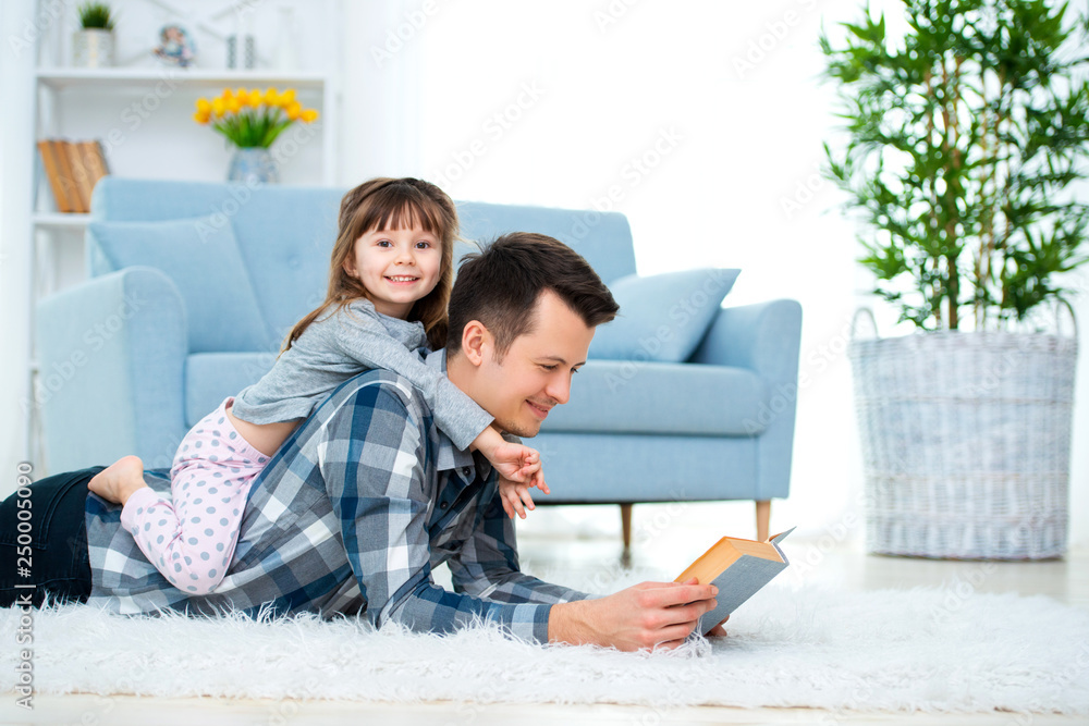 Happy family and father's day concept. Dad with daughter spending time togetherness at home. Cute little girl on dad's back lying on warm floor Happy family and father's day concept. Dad with daughter spending time togetherness at home. Cute little girl on dad's back lying on warm floor