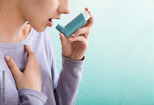 Young woman using inhaler against asthma on color background