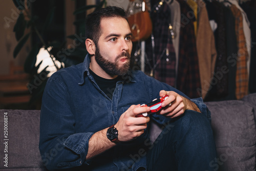 Portrait of a handsome man playing video games in his apartment, stressed about the outcome.