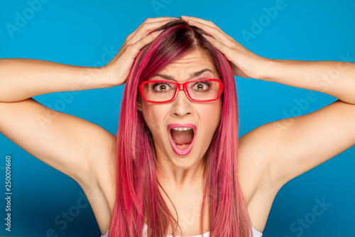 Shocked woman with a pink hair and glasses on blue background