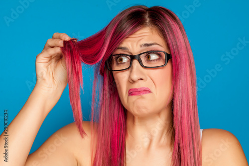 Unhappy woman looking her pink hair on blue background