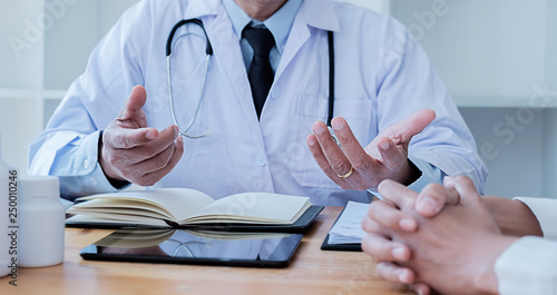 Patient listening intently to a male doctor explaining patient symptoms or asking a question as they discuss paperwork together in a consultation