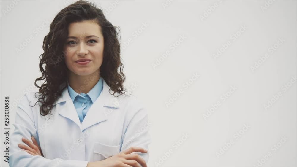 Portrait of happy young smiling girl doctor. Dressed in a white robe. Evenly standing with crossed hands on a gray background. Portrait of happy young smiling girl doctor. Dressed in a white robe. Evenly standing with crossed hands on a gray background.