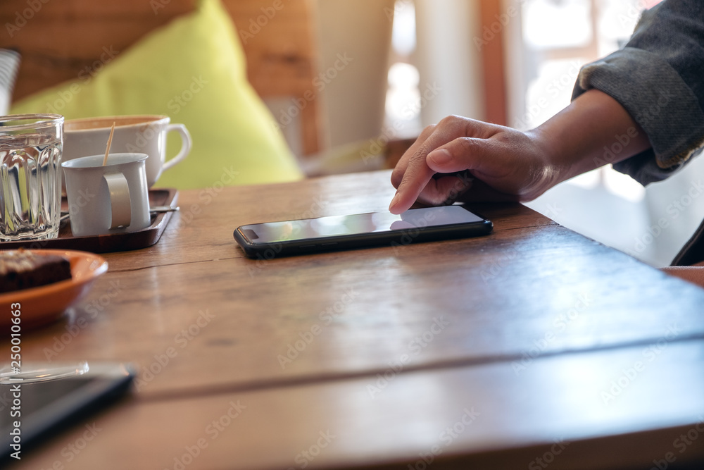A woman's hand using and touching a smart phone screen with coffee cup on wooden table in cafe A woman's hand using and touching a smart phone screen with coffee cup on wooden table in cafe
