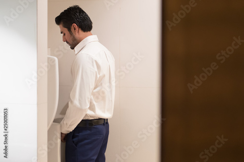 Asian man urinating in toilet; portrait of Indian man using water closet, WC for peeing; concept of health care, prostate cancer, urethritis, UTI or urinary tract infection; Asian adult man model