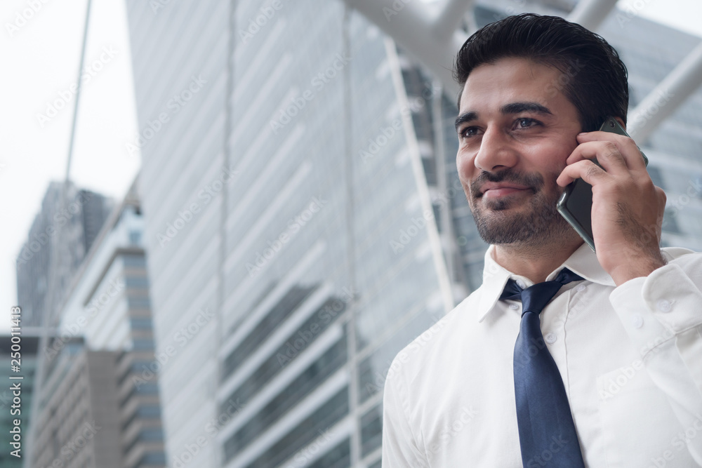 Fototapeta premium happy asian business man talking smart phone; portrait of happy smiling successful Asian, Indian businessman talking via smart phone; negotiation, business deal, transaction, communication concept