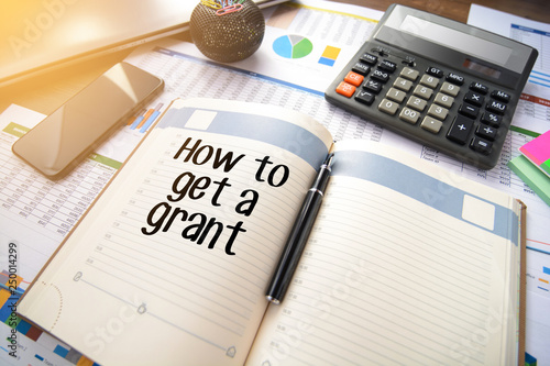 Business accessories, smartphone calculator, laptop, reports and diary with text How to get a grant photo