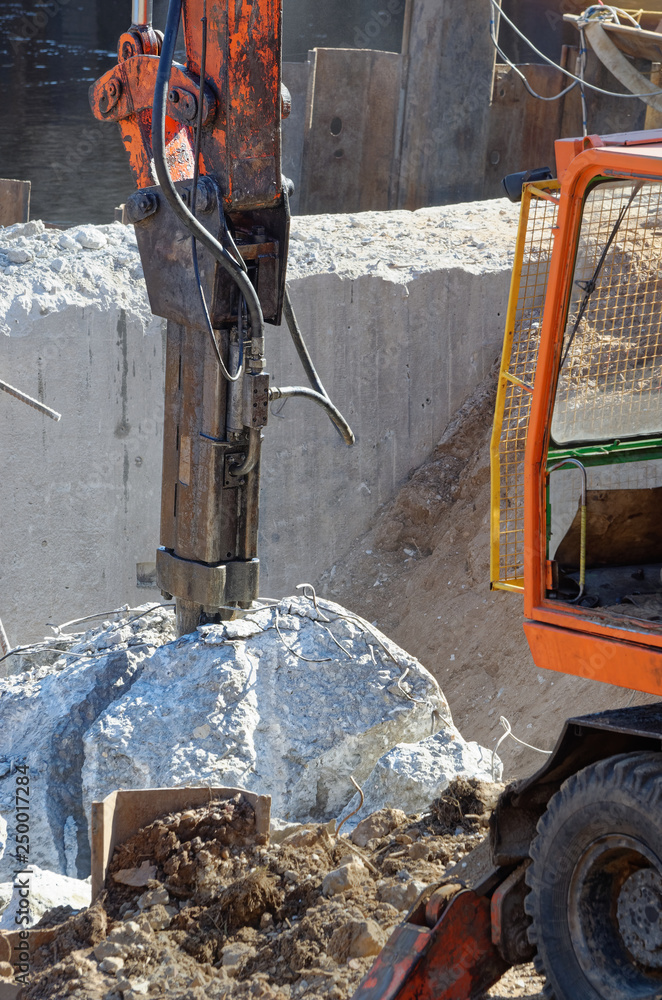 Fototapeta premium Demolition excavator with hydraulic hammer resting between two pieces of just divided concrete block